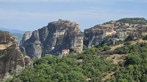 Panoramic view of Meteora monasteries perched atop massive cliffs surrounded by green valleys.