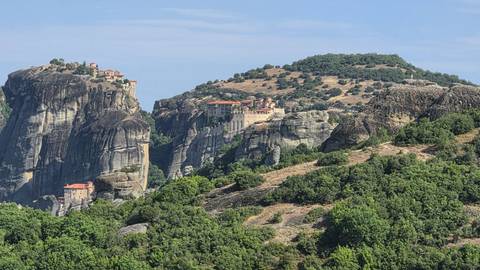 Rock formations of Meteora with ancient monasteries nestling on cliff tops amid lush greenery.