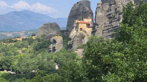 Rocky pillars and distant valley views of Meteora partially framed by tree branches.