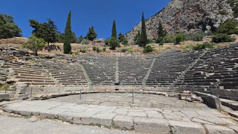 Stone seating tiers of the Ancient Theatre of Delphi curve around the orchestra with a cliff backdrop.