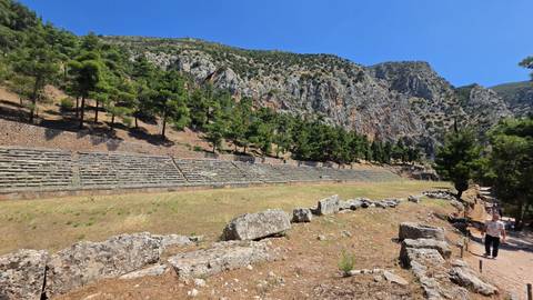 Long rectangular ancient stadium at Delphi set against rocky hills and pine-covered slopes.