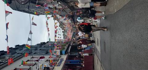 Busy pedestrian street lined with pubs and cafes, colorful international bunting strung overhead and crowds strolling