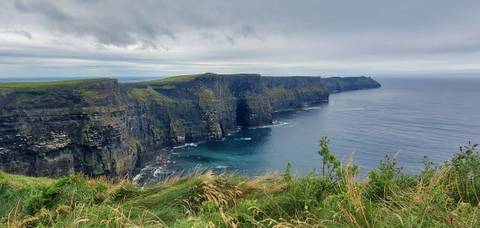 Dramatic sheer sea cliffs plunging into the Atlantic with rolling grass tops under a grey sky