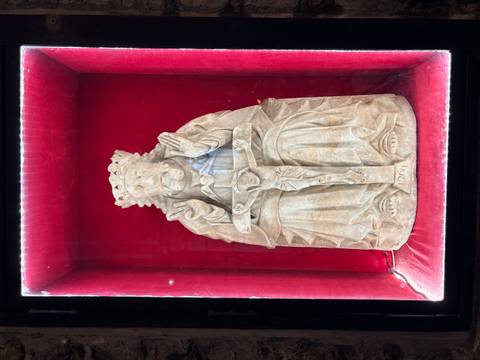 Intricately carved religious statue displayed in a red velvet-lined glass case