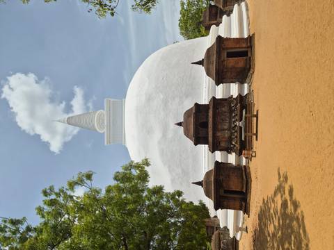Brilliant white stupa with three small brick shrines at its base rising against a bright blue sky.