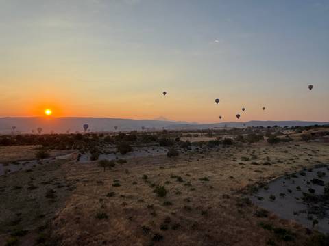 Hot-air balloons drift over Cappadocia’s golden grasslands at sunrise.
