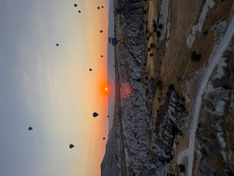 Sun rises over rugged Cappadocian landscape dotted with soaring hot-air balloons.