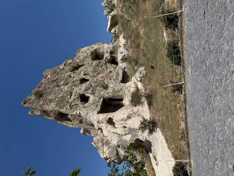 Eroded rock outcrop with ancient cave dwellings and openings against a deep blue sky.