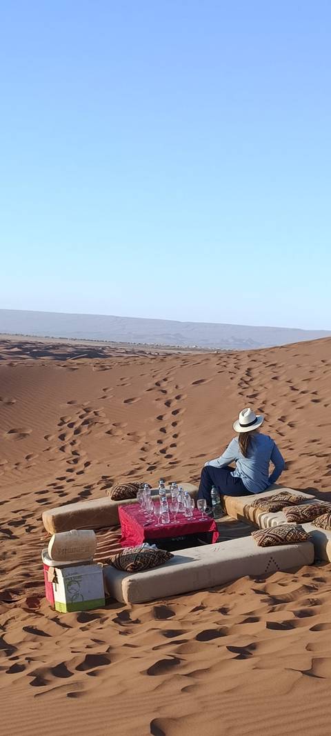 Traveller in a wide-brimmed hat walking along vast red sand dunes stretching toward a distant ridge.