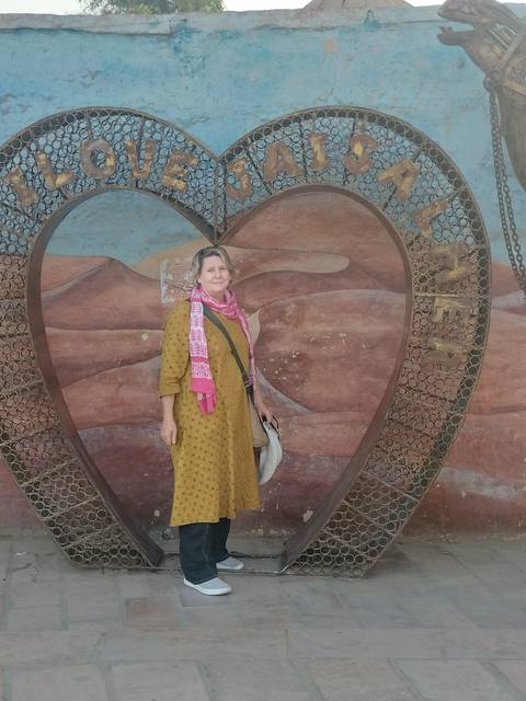 Woman posing in front of a large metal heart-shaped sculpture set against a painted desert backdrop.