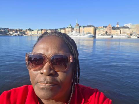 Selfie of a woman wearing sunglasses with Stockholm waterfront and historic buildings in the background.