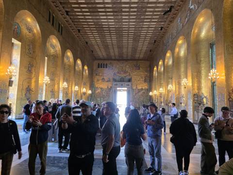 Interior of Stockholm City Hall’s Golden Hall with ornate mosaics, chandeliers and many visitors.