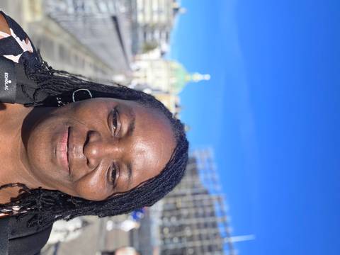 Outdoor selfie with bright blue sky and a domed building partially visible in the blurred background.