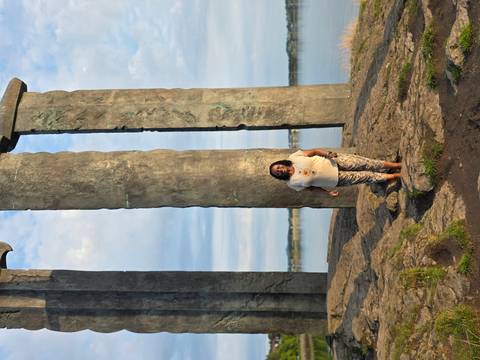 Woman poses in front of three towering Viking-sword monuments beside a calm fjord.