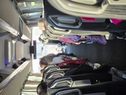 Interior view down the aisle of a tour coach with seated passengers and overhead luggage racks.