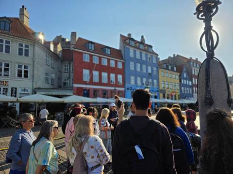 Tour group stands on a sunny square facing rows of colorful old houses with café terraces.