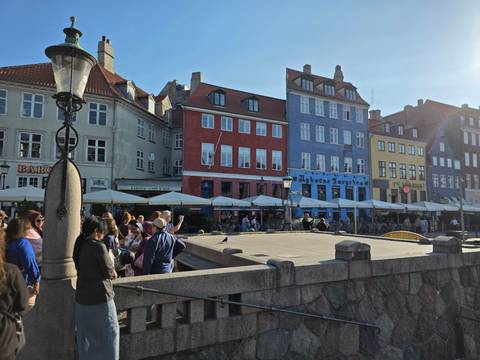 Wide shot of a canal bridge with busy tourists and colorful waterfront buildings under bright sun.