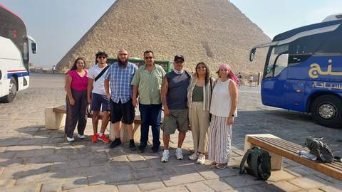 Tour group poses in front of the Great Pyramid with tour buses nearby