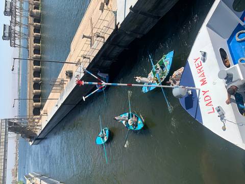 Small rowboats approach a cruise ship in a Nile lock, engaging in lively river trade