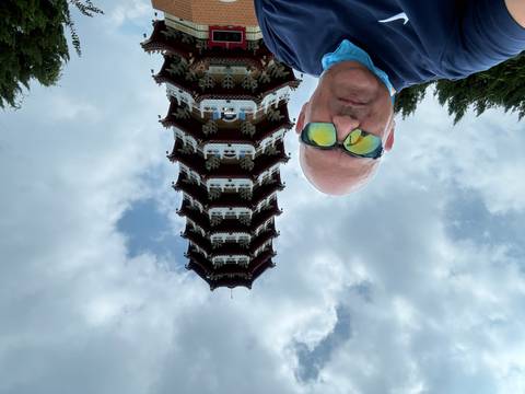 Selfie of man wearing sunglasses in front of ornate pagoda tower under cloudy sky