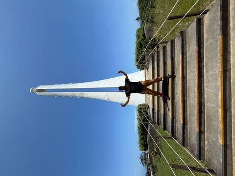 Man posing triumphantly on stairs before tall white monument under clear blue sky