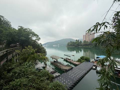 Serene lake with moored boats and forested hills in misty weather