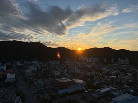Sunset over city blocks with dramatic clouds and sun dipping behind hills