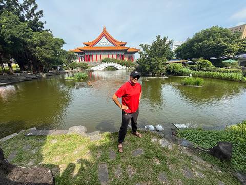 Man standing beside pond with traditional Chinese hall and arch bridge