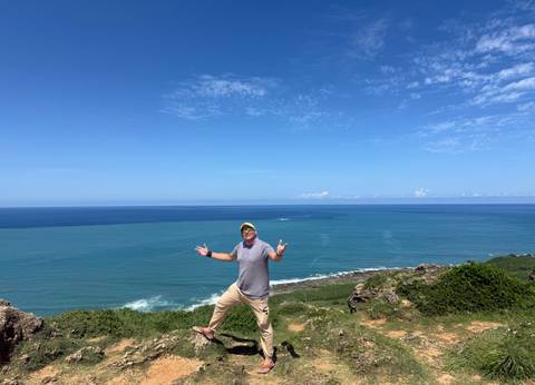 Man standing on coastal cliff overlooking vast blue sea and sky