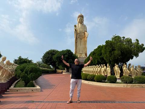 Visitor posing before towering golden Buddha statue lined with rows of small statues