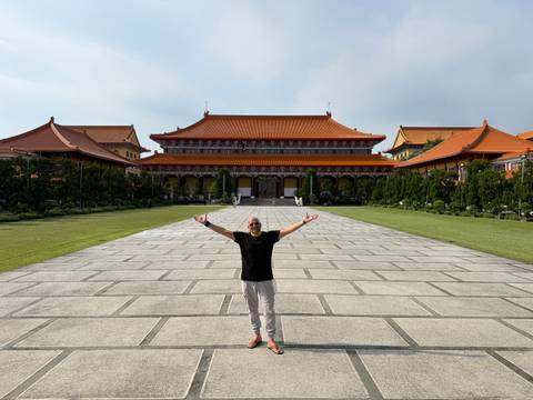 Man posing happily on grand plaza leading to ornate Chinese temple complex