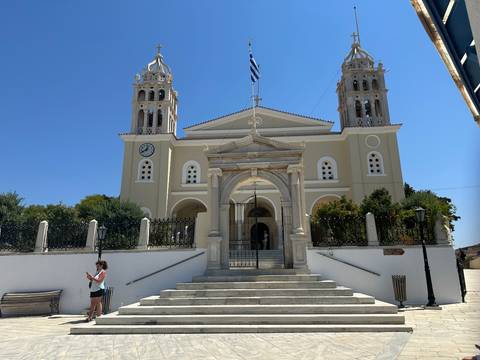 Neo-Classical Greek church with twin bell towers and Greek flag flying overhead.
