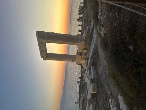 The Portara gateway of Naxos silhouetted against a colorful Aegean sunset.