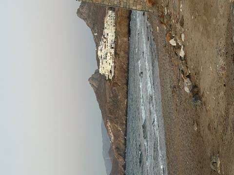 Rocky shoreline with small white village clinging to a cliff above choppy sea.