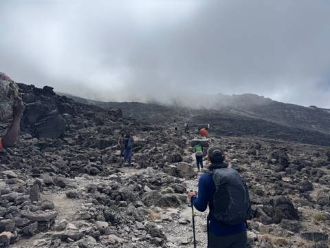 Hikers trek across a barren lava field under low cloud on the slopes of Mount Kilimanjaro
