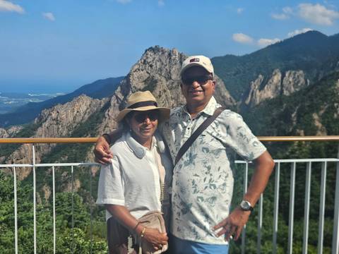 Couple smiles on a mountain viewing deck with rocky peaks and forested valleys behind