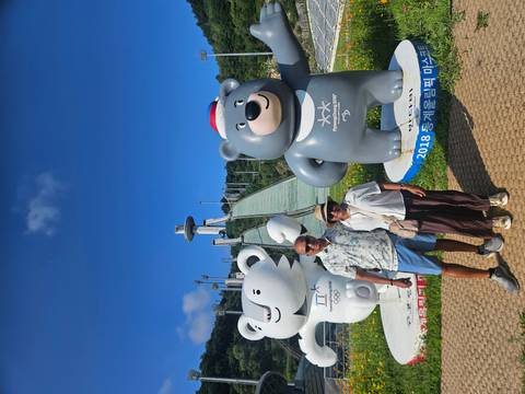 Travelling couple poses with Winter Olympic bear mascots before a ski jump tower