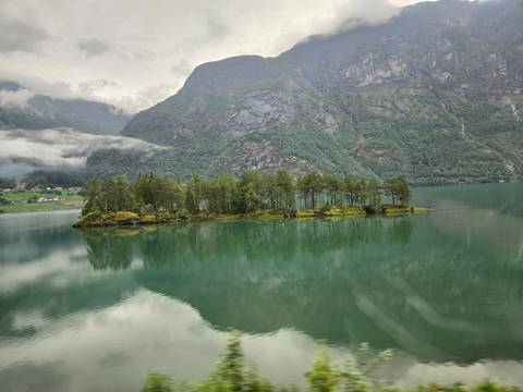 Small forested island sits in a misty green lake surrounded by towering mountains