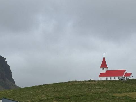 Small white church with a bright red roof and spire standing alone under a grey sky.