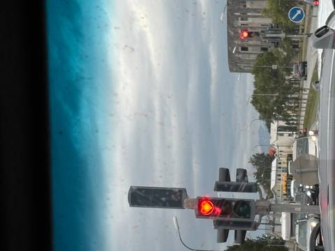 View through a car windshield toward a traffic light and urban street, with dirty glass spots visible.