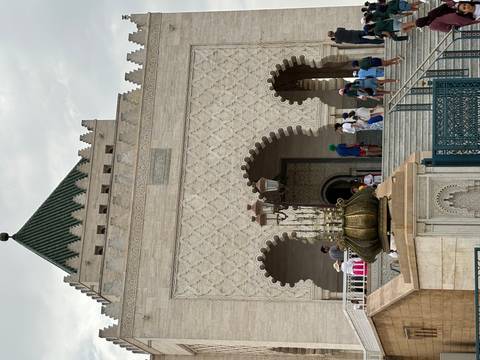 Facade of the Mausoleum of Mohammed V with ornate arches and visitors climbing steps.
