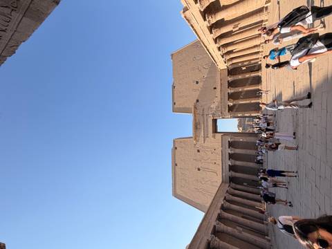 Spacious courtyard and pylon entrance of Edfu Temple with tourists exploring under blue sky.