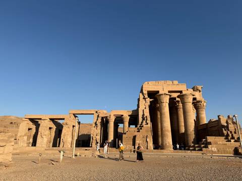 Ruins of Kom Ombo Temple with towering sandstone columns silhouetted against deep blue sky.