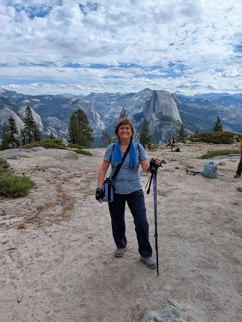 Hiker smiling on granite lookout with Half Dome and Yosemite high country behind.