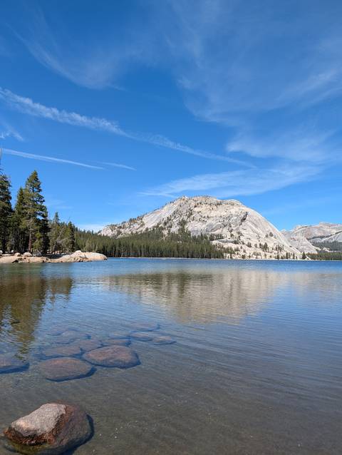 Crystal lake reflecting granite dome and pine forest beneath bright blue Yosemite sky.