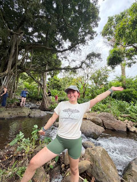 Happy hiker raising an arm in a lush stream-side jungle while others explore the rocks nearby.