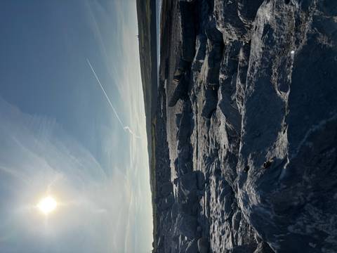 Rocky coastal landscape under low sun with jet trail across the sky.