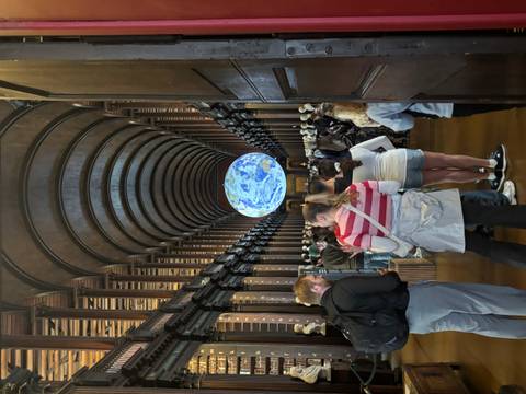 Crowded interior of Trinity College Old Library with illuminated earth globe exhibit.