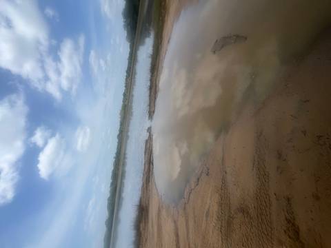 Blurry view of a sandy bank and shallow water lagoon under a partly cloudy sky.