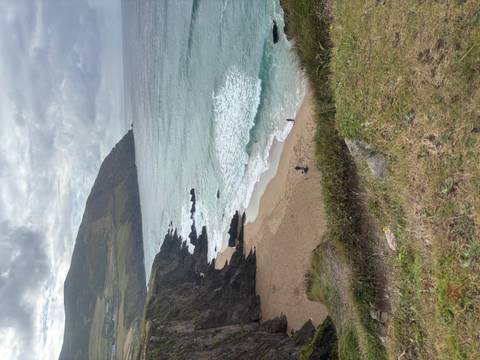 Dramatic coastal cliff with secluded sandy beach and rolling waves.